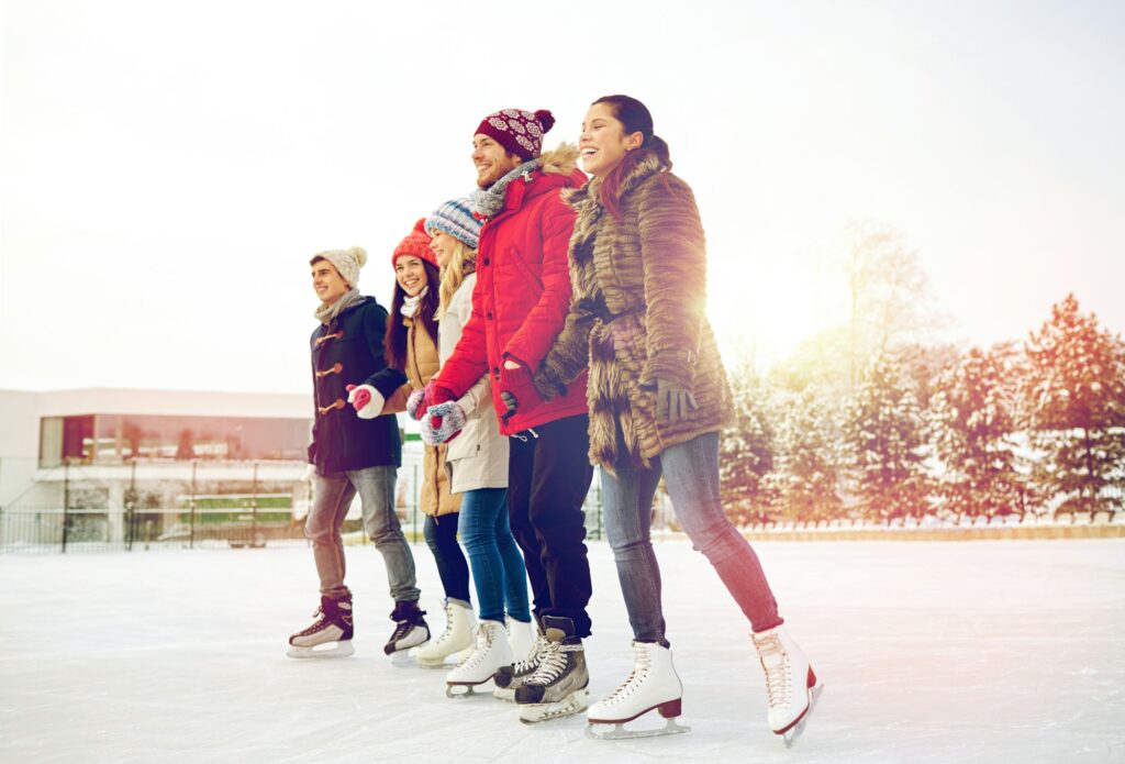 happy friends ice skating on rink outdoors